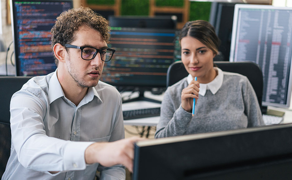 Two men and women talking in an office while looking at computers