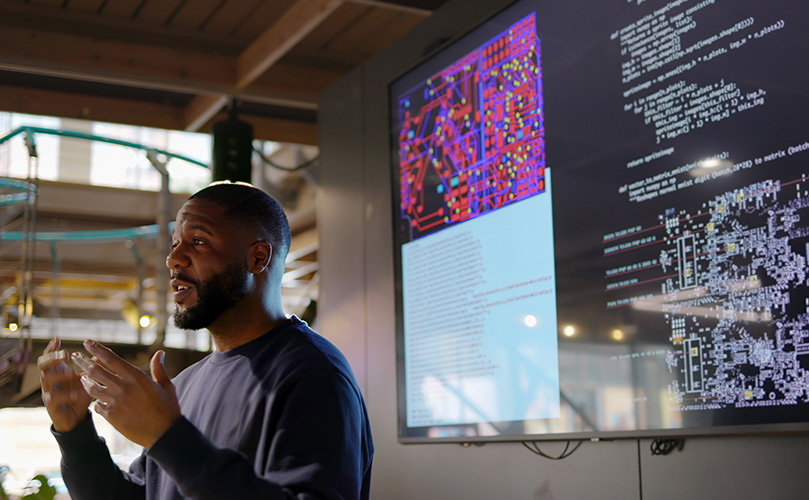 Image of a male technician speaking in front of a display monitor