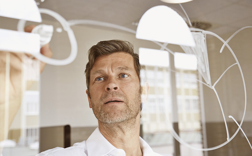 Businessman drawing diagrams on glass pane in office.