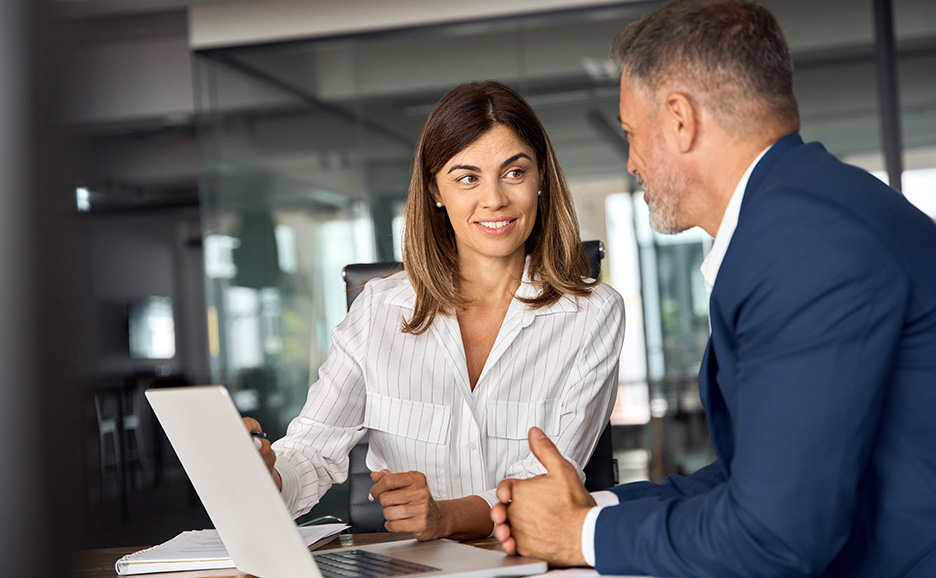 オフィスで、女性が男性にラップトップを見せながら会話しています。