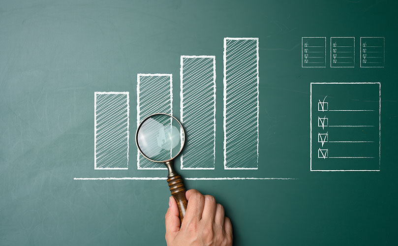 黒板に描かれた成長を示すグラフとチェックリストを虫眼鏡で確認する手。