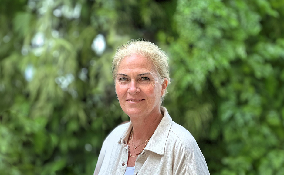 A woman in a white shirt stands amidst green plants