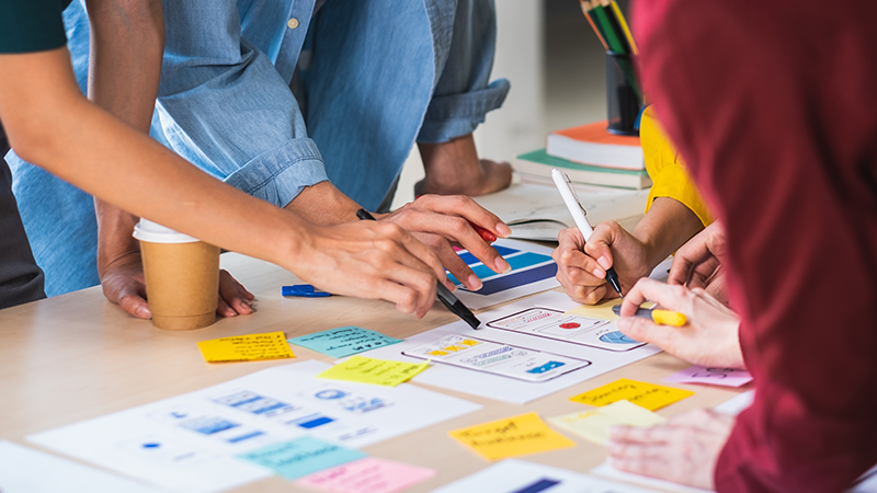 A group of professionals seated at a table, engaged in teamwork and project planning with materials spread out.