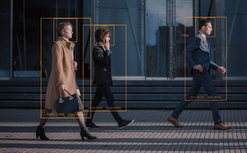 Three people walking in business attire, framed by orange rectangles for object detection. They appear focused and purposeful on a city sidewalk.
