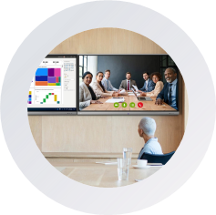 icon A diverse group of people seated in a conference room, engaged in discussion with a video screen displaying information.
