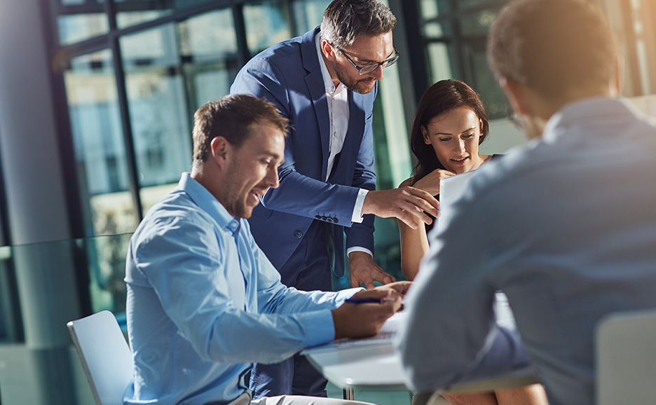 ビジネス会議で、男性がノートに書き込み、別の男性が説明し、女性が耳を傾けています。