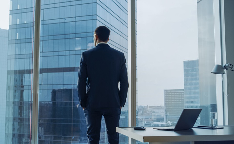 A man in a suit gazes out a city-view window, reflecting on the urban landscape beyond.