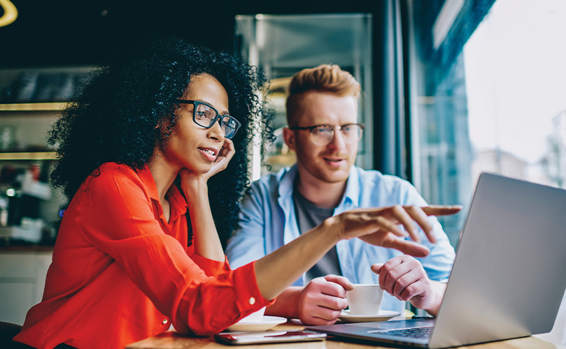 Eine Frau und ein Mann sitzen in einem Café und betrachten gemeinsam einen Laptop