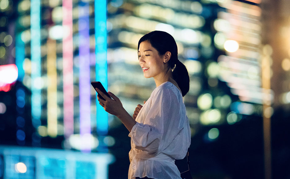 夜外でスマートフォンを見ている笑顔の女性