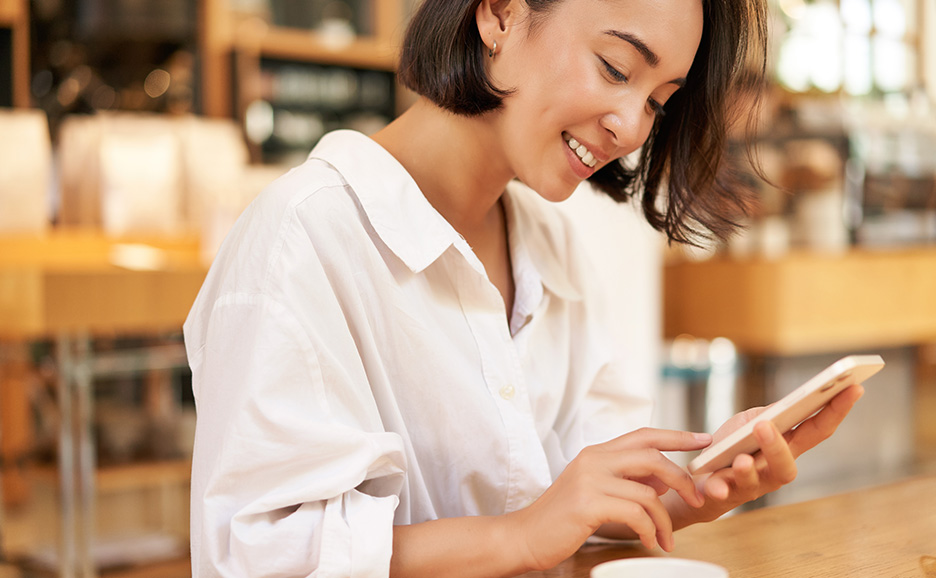 カフェでスマートフォンを操作している笑顔の女性