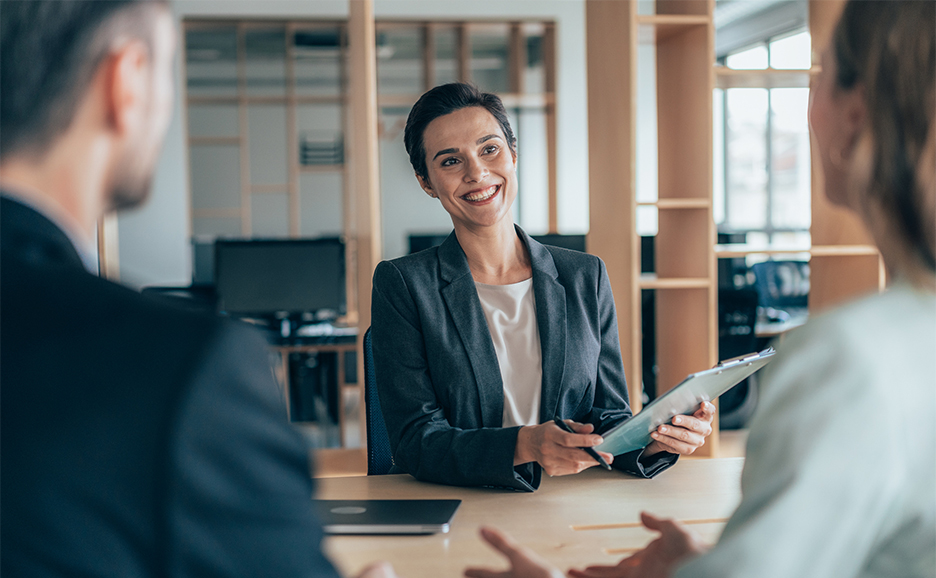A woman in a suit sits at a table and smiles at a man sitting across from her.