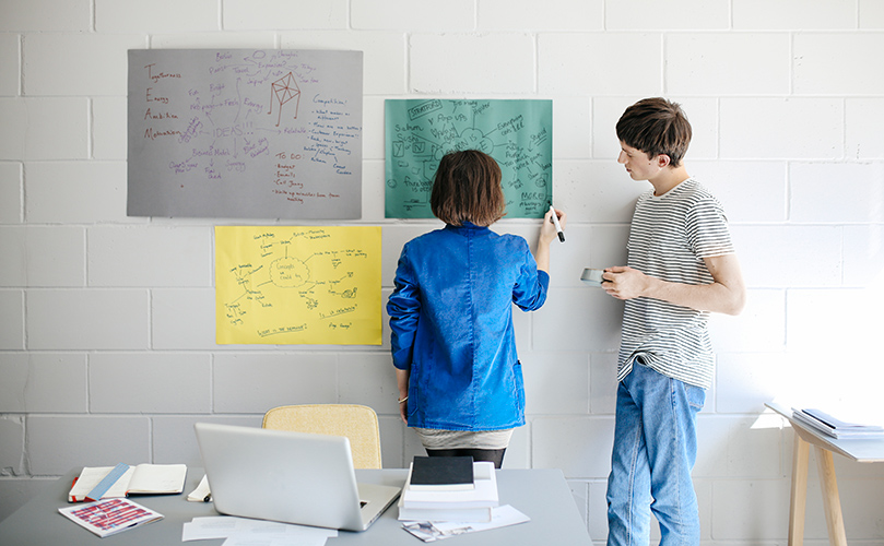 Two individuals standing in front of a whiteboard, engaged in discussion or presentation.