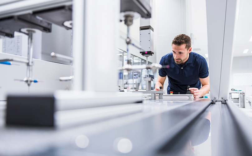 A man operates a machine in a factory, focused on his task amidst industrial equipment and surroundings.