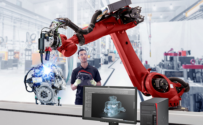 A man focused on his computer with a robot visible in the background, highlighting technology in a work environment.