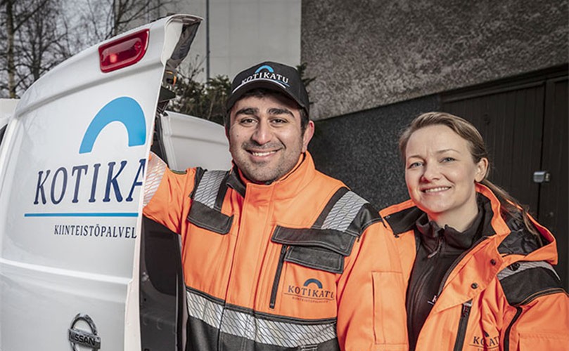 A man and woman stand beside a parked van, smiling and engaged in conversation.
