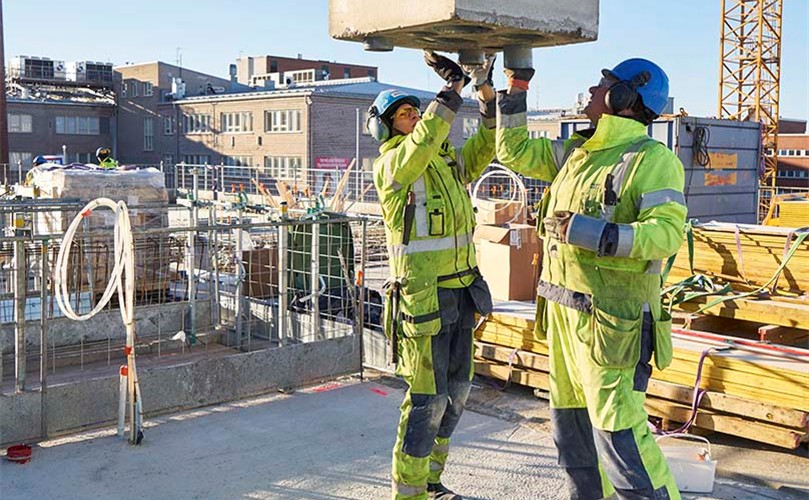 Two men in safety gear are lifting a large concrete block at a construction site.
