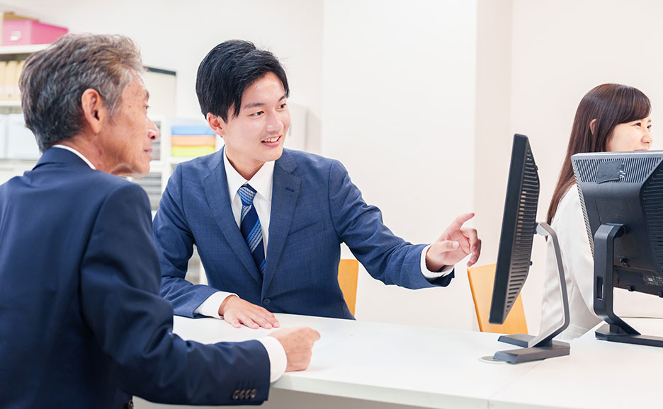 パソコン画面を指さしながら説明する男性と説明を受ける男性