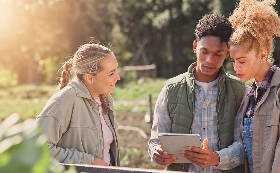 畑でタブレットを見ている3名の男女