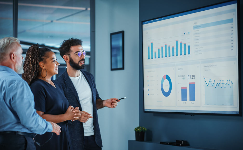 There are men and women arguing in front of a monitor with graphs and tables