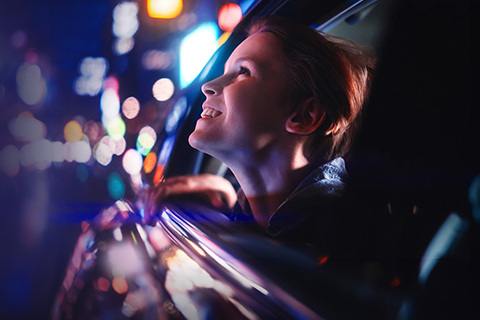 ネオン光る夜の街を車の窓から眺めている子供