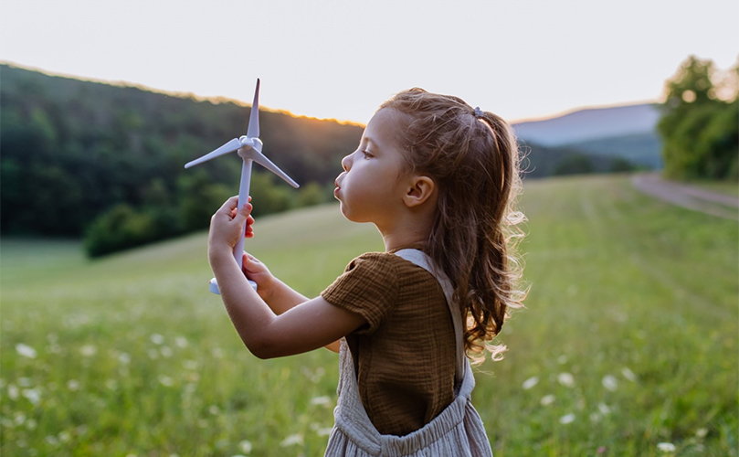 A little girl stands in a field, joyfully holding a colorful windmill that spins in the breeze
