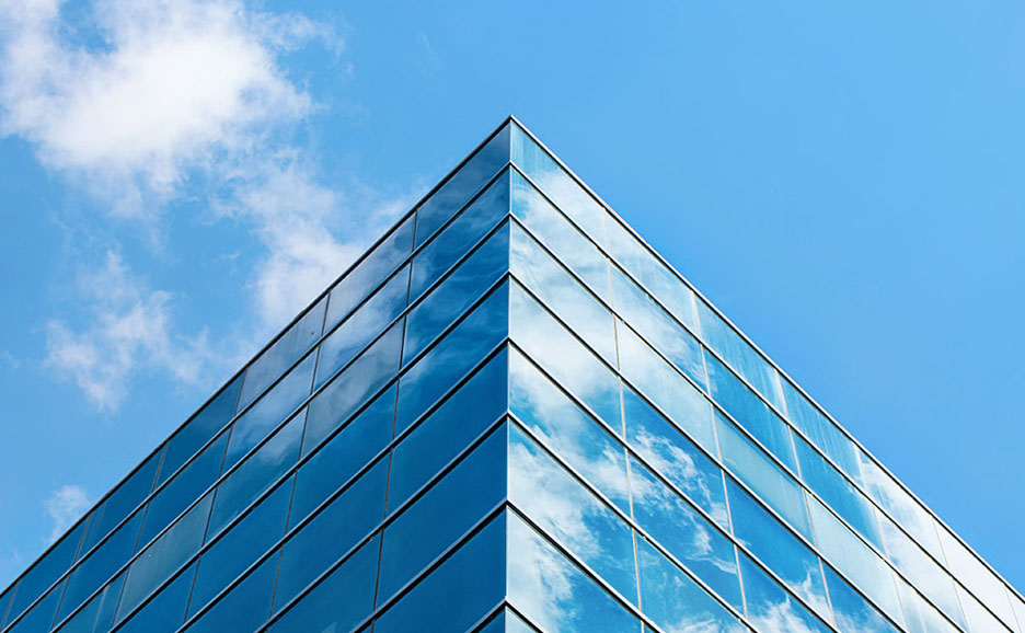 The corner of a modern glass building reflecting a blue sky and white clouds