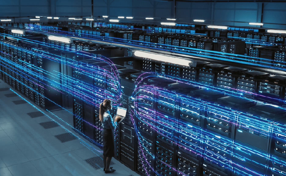 A woman operating a laptop in a data center lined with servers