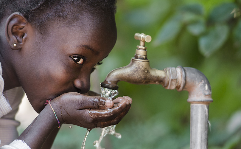 A young girl joyfully drinks water directly from a tap