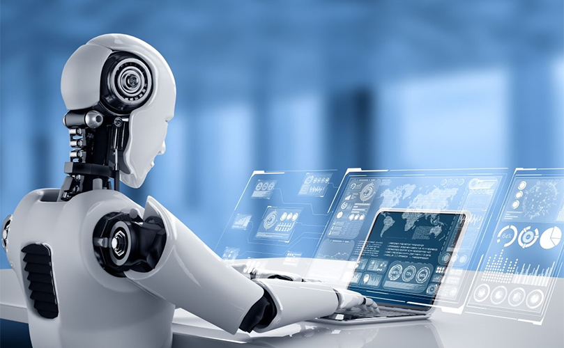 A robot seated at a desk, focused on a laptop