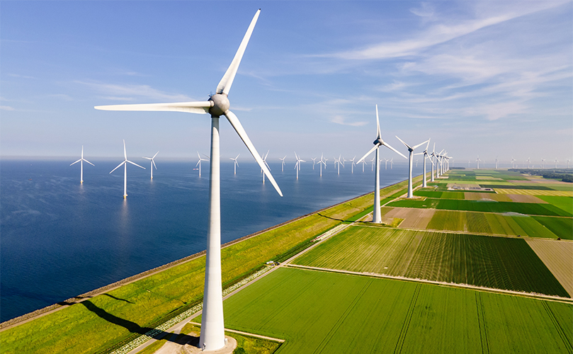 A wind farm featuring multiple tall wind turbines against a clear blue sky. 