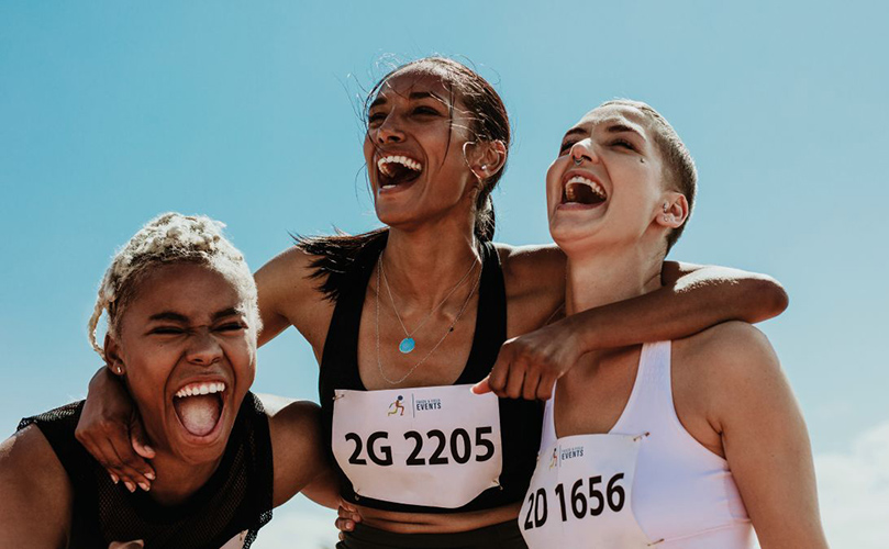 Three women joyfully laughing and smiling while running together outdoors.