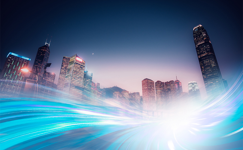 A blue light trail arcs in front of a city skyline, highlighting the urban landscape against a darkening sky.