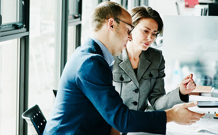オフィスで書類を見ながら話し合う男女。