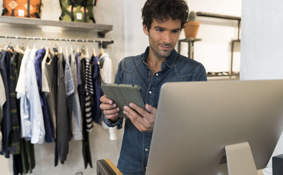 衣料店舗でタブレットとPCを操作する男性