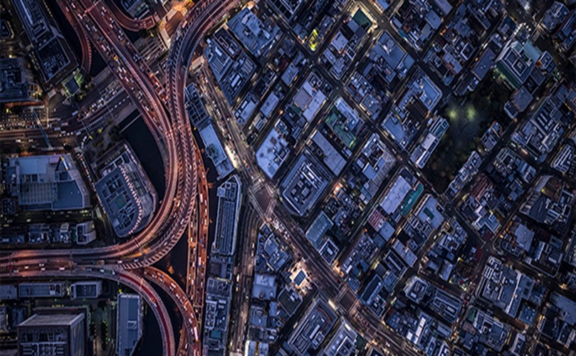夜空から見下ろした都市風景。光が輝く高速道路と建物が並んでいます。