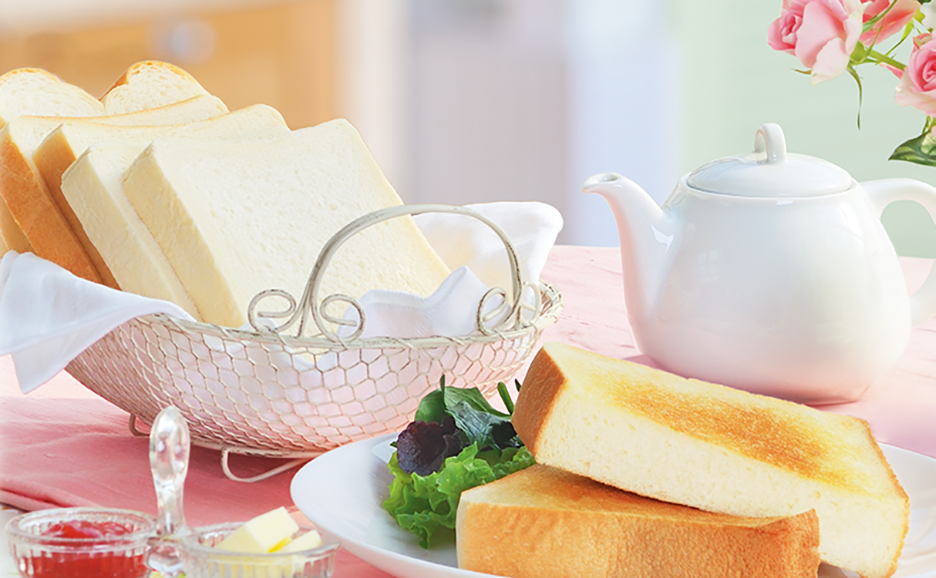 ティーポットとバラの花が飾られたテーブルに、焼いたパンと焼いていないパン、ジャムとバターが置かれています。