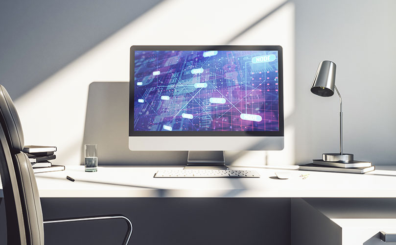 抽象的なデジタルネットワーク図がデスクトップモニターに表示されている、モダンなオフィスワークスペースの画像。