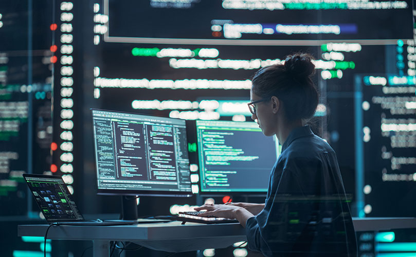 モニターの前に座ってプログラミングをする女性。