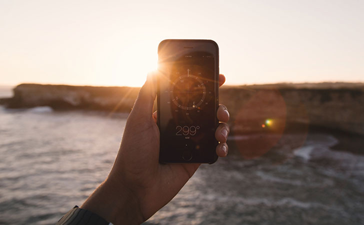 夕日を背景にスマホの羅針盤アプリを使う手元。