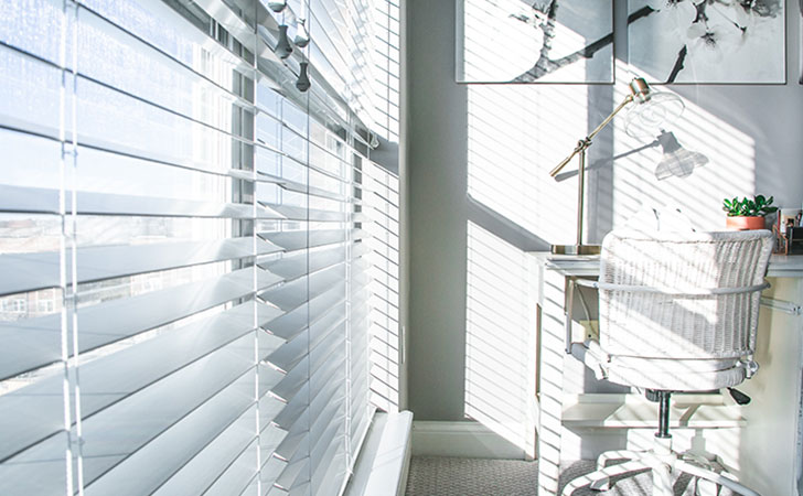 日差しが差し込む部屋のデスクと椅子、ブラインドの影。