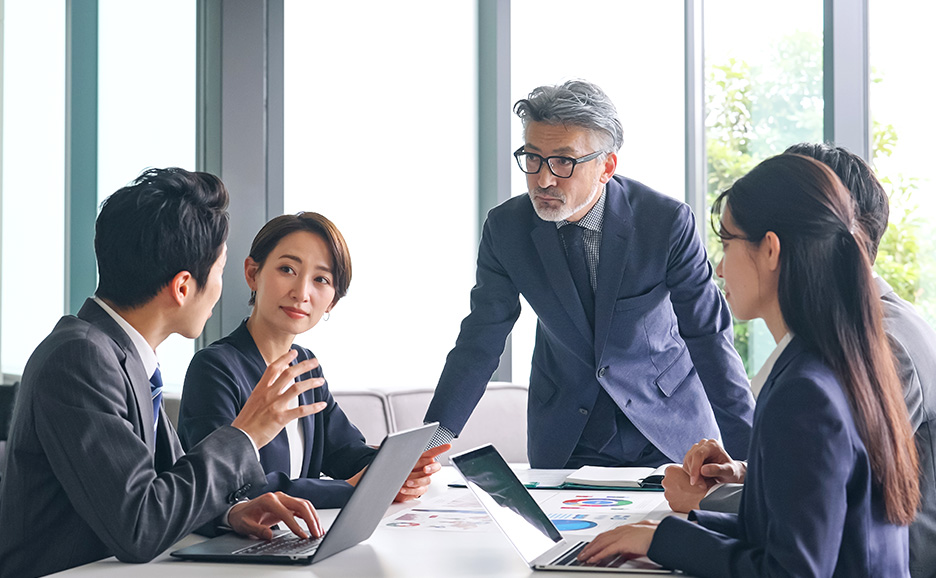 会議室で資料を囲み議論するビジネスチームの打ち合わせ風景