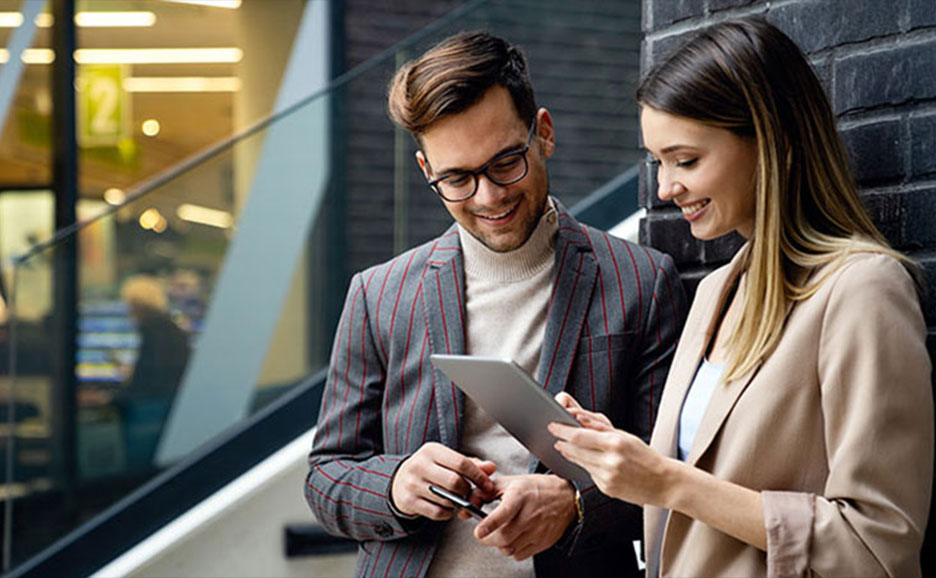 Zwei Kolleginnen und Kollegen im Bürobereich betrachten gemeinsam ein Tablet.