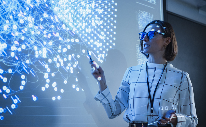 An image showing a woman with glasses pointing at a screen with many dots.