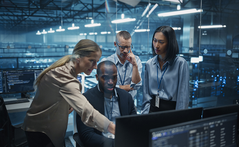 Diverse team of IT professionals collaborating on computer screens in a server room