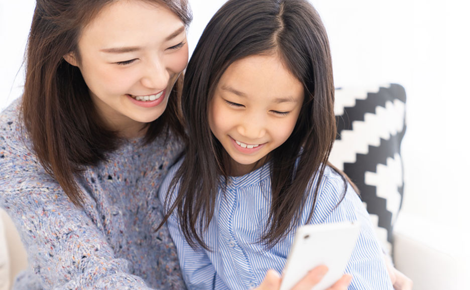 笑顔の母と娘がスマートフォン画面を眺めている