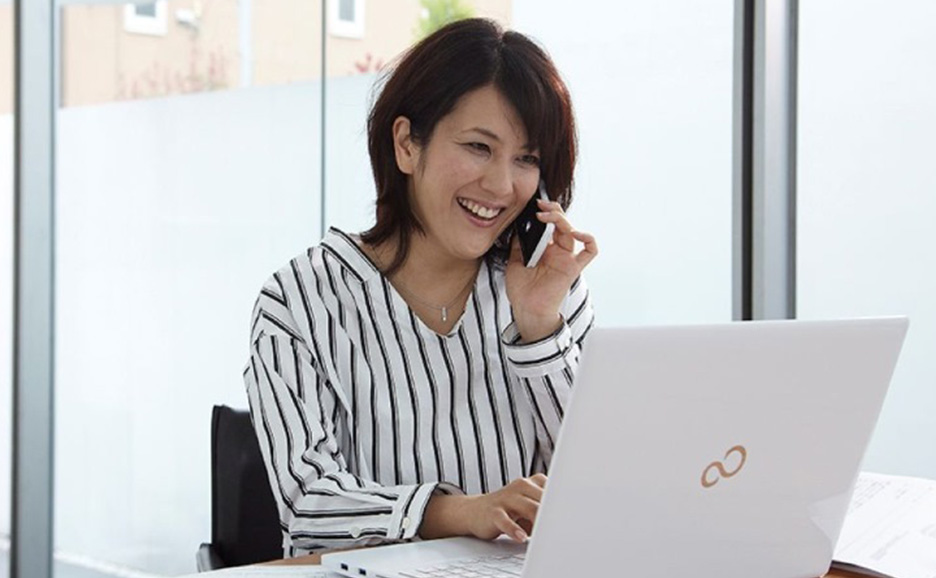 ノートパソコン画面を見ながら電話をする女性