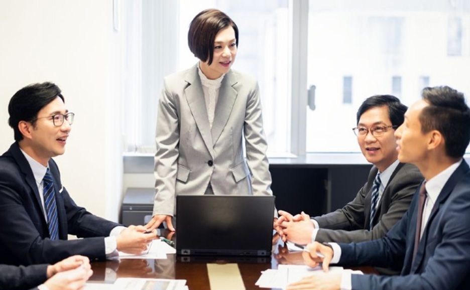 席を立って話す女性を中心に会話する男性4名