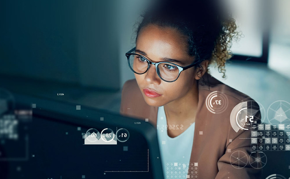 眼鏡をかけ、多くのデータが重ねて表示された画面を見ている女性。