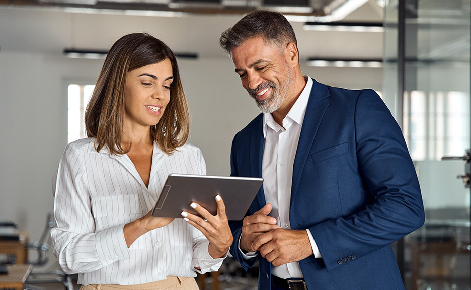 Two business people smiling and talking while looking at a tablet