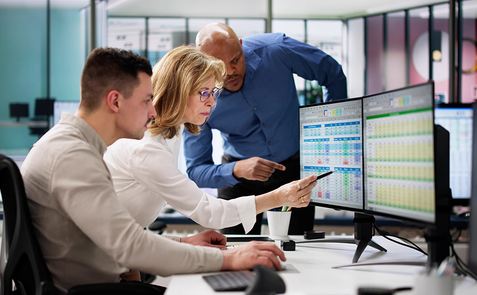 Three business people consulting over data displayed on multiple monitors